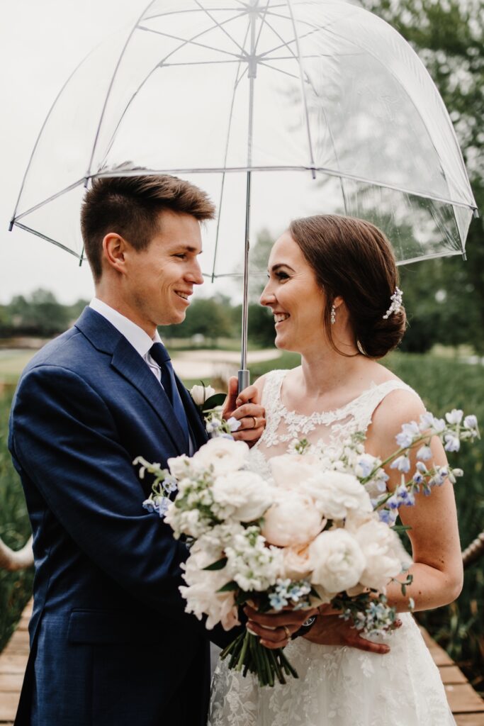 Bride and groom under umbrella at golf course wedding