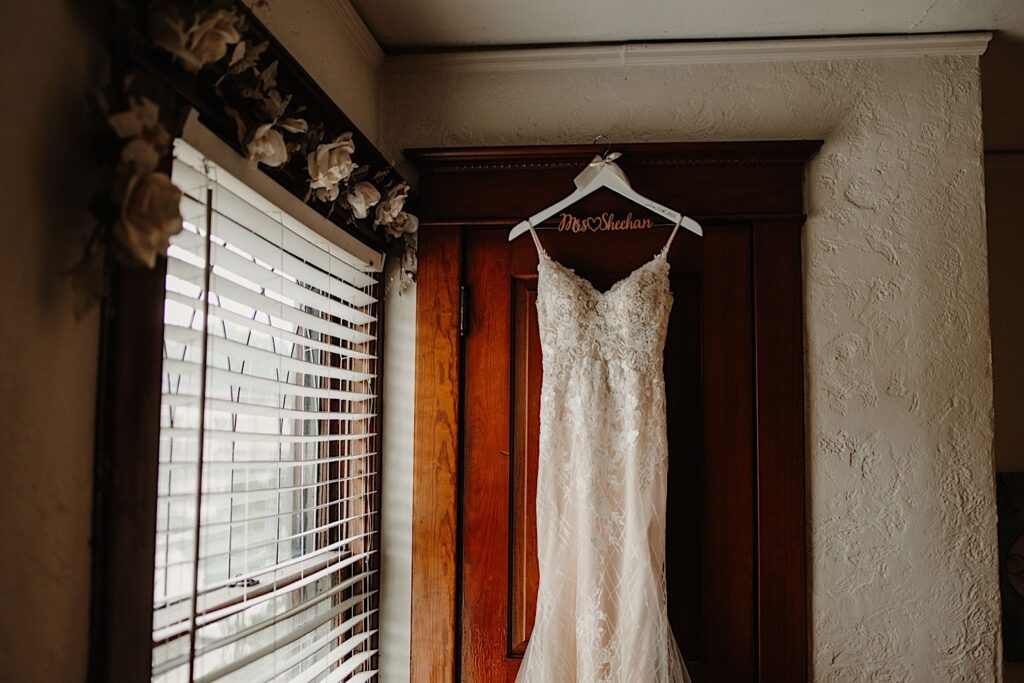 A lace wedding dress hung on an antique door with a white engraved hanger on the morning of a wedding.