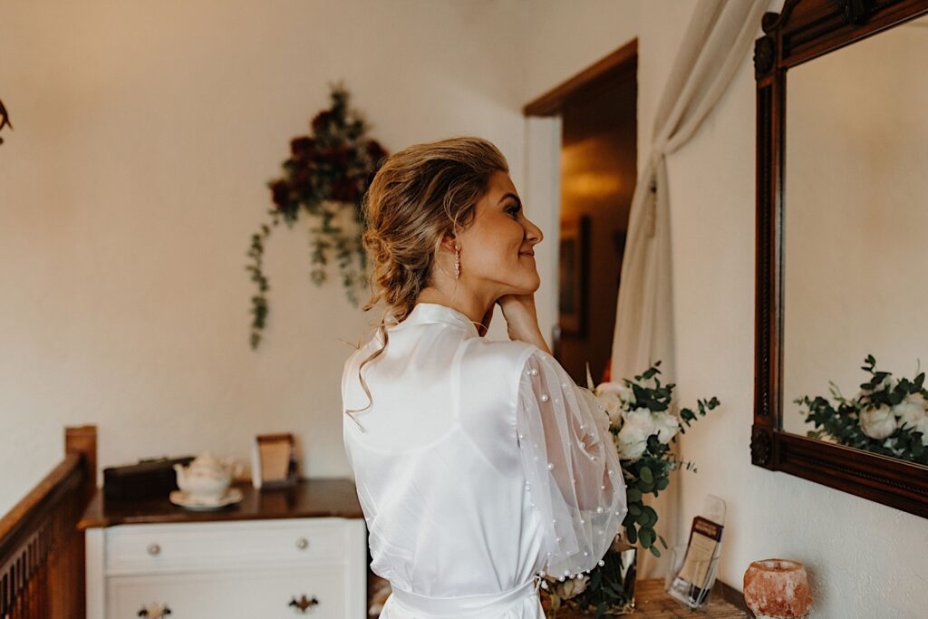 A bride smiles and looks in the mirror as she puts on her earrings in the Chicago Inn she is getting ready in.