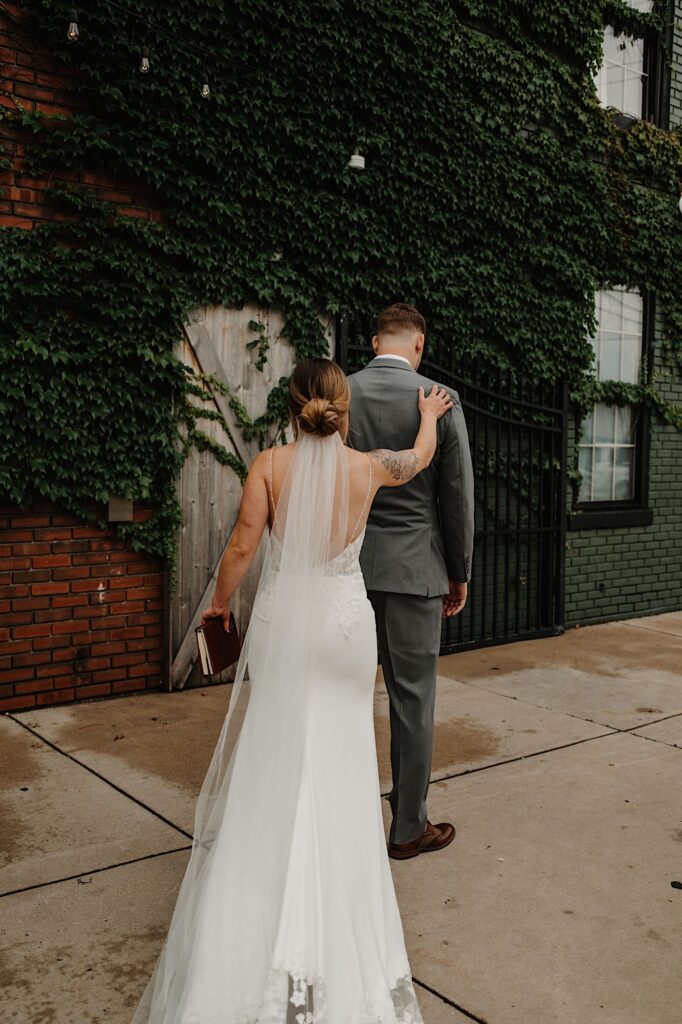 A bride taps the groom on the shoulder for him to turn around for their first look outside their wedding venue