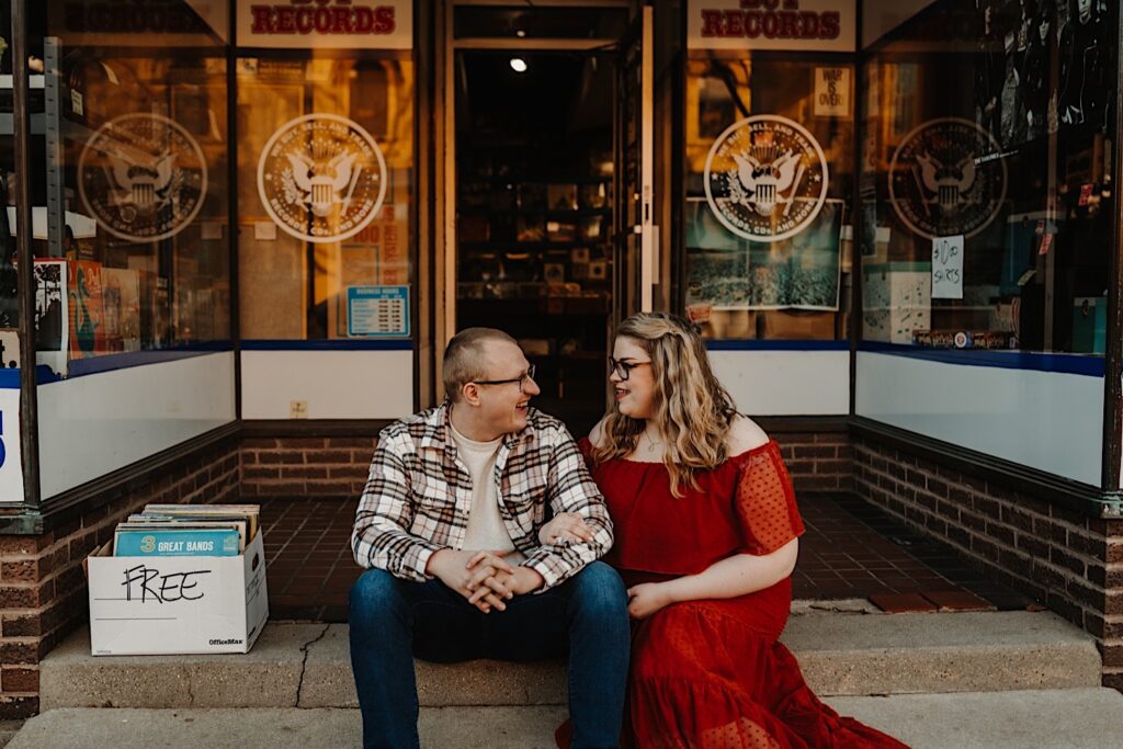 A couple poses for their engagement photos sitting outside of North Street Records in Bloomington Normal Illinois.