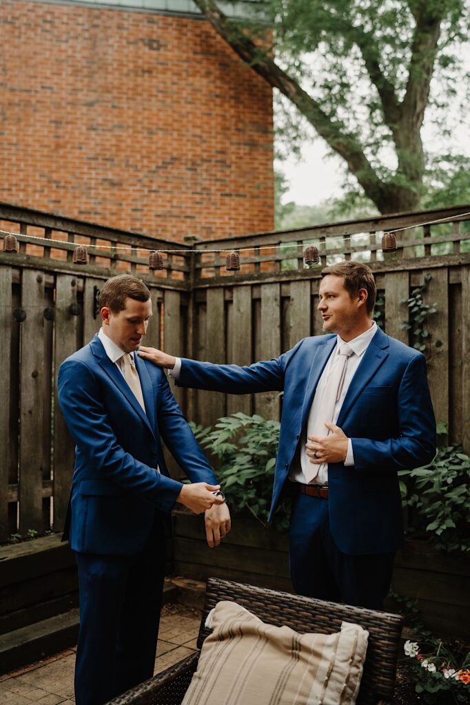 A groom stands getting ready with his groomsmen on an overcast day in Chicago.  They stand outside on their back porch in blue suits and champagne colored ties.