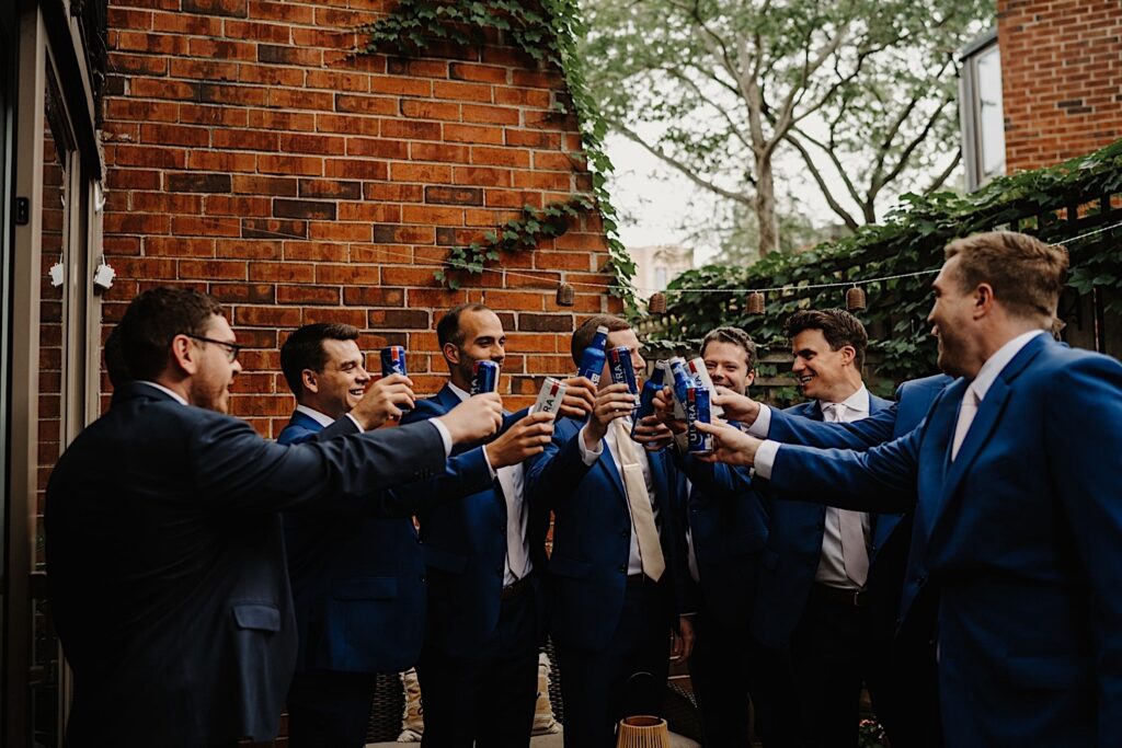 The groom makes a toast with his groomsmen with brick and ivy in the background.  They are standing outside his Chicago home on an overcast day.