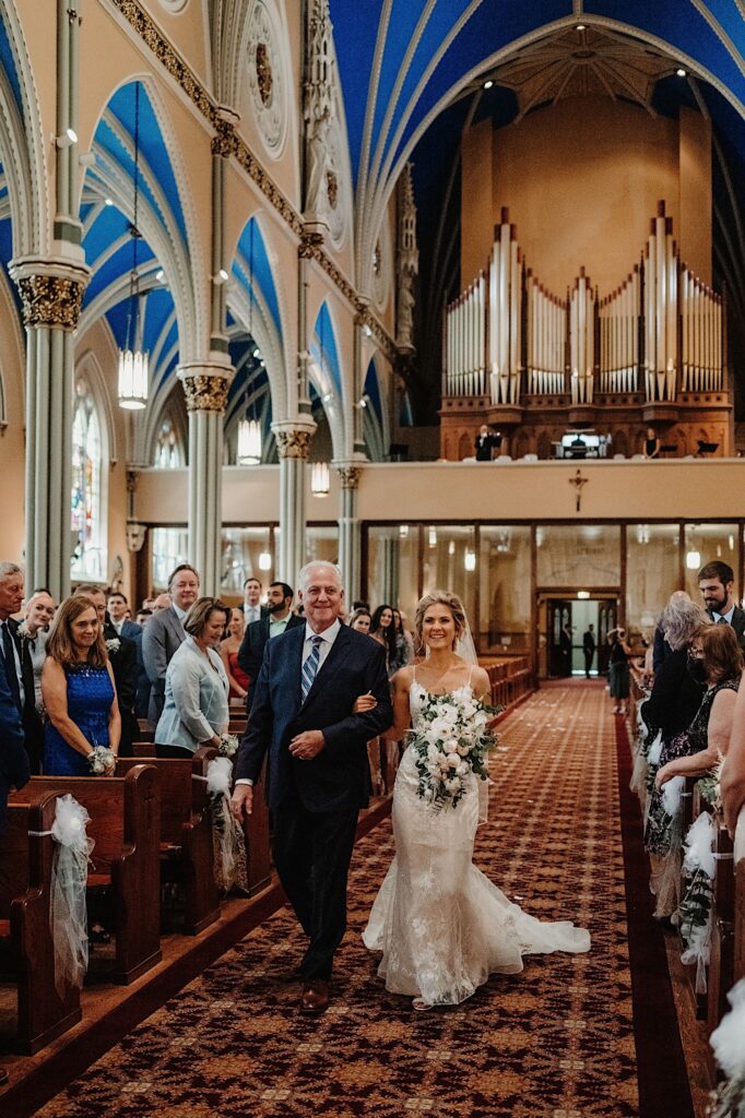 A bride and her father walk down the aisle towards her groom on their wedding day at St Alphonsus church in Chicago.