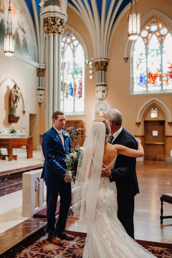 The father of the bride passes off his daughter to the groom during their Chicago wedding ceremony at St. Alphonsus Church.