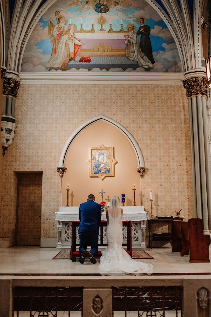 A bride and groom kneel on kneelers and pray to the sacred mother during their wedding ceremony at St. Alphonsus Church in Chicago.