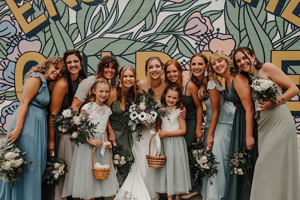 A bride and her bridesmaids and flower girls pose together for a portrait in front of a mural