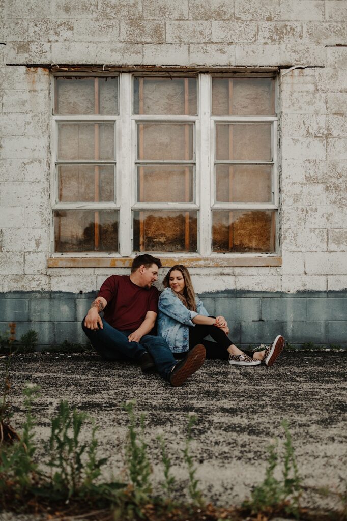 A couple sits in front of a large window and blue and white brick wall at an old gas station in Central Illinois for their engagement session.
