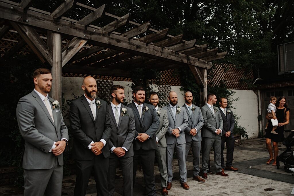 A groom stands with his groomsmen at his side before his wedding ceremony at the Ivy House's outdoor space