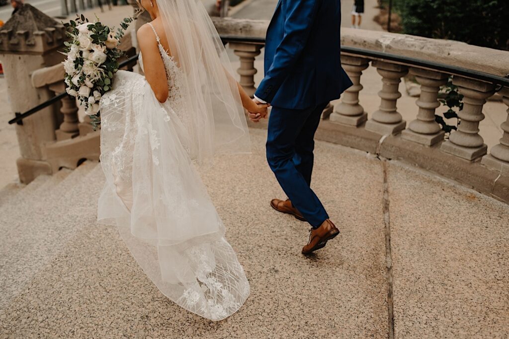 An image of the bride and groom holding hands and walking away from the camera down the steps at St. Alphonsus church in Chicago.
