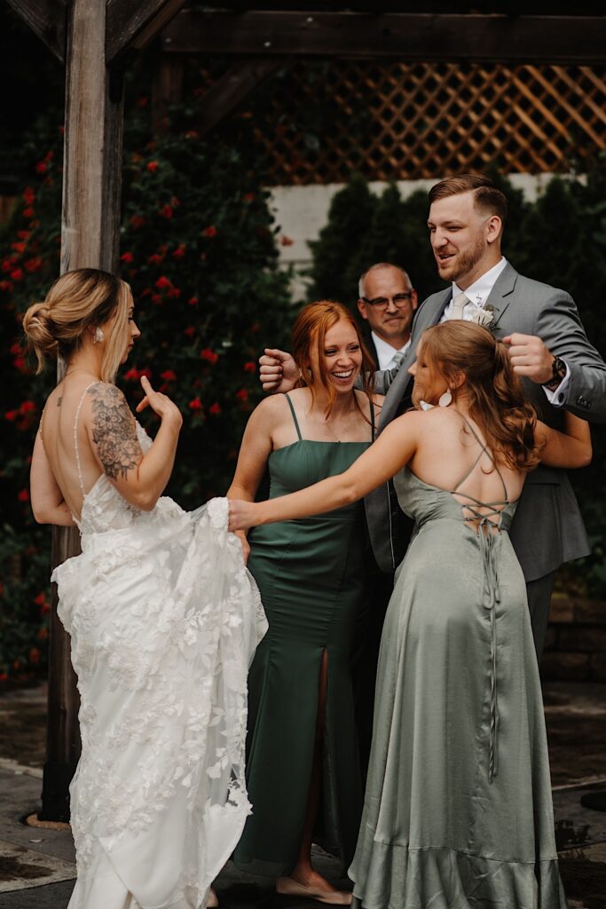 A groom laughs as he is hugged by bridesmaids as one tries to drag the bride to him.