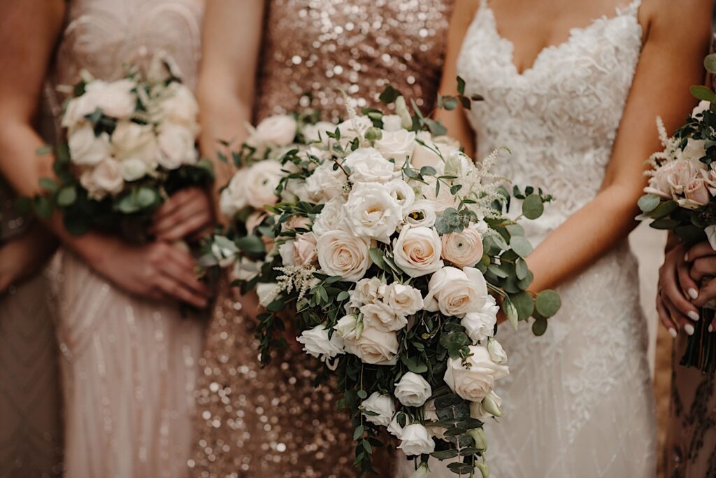 A close up image of the brides bouquet surrounded by her and her bridesmaids.  You can mostly see their dresses which are white and champagne colored.