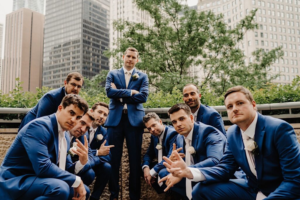 The groom and his groomsmen pose as if they are making an album cover, with the grooms arms crossed and all of the groomsmen squatting.  They stand next to the Chicago Riverwalk.