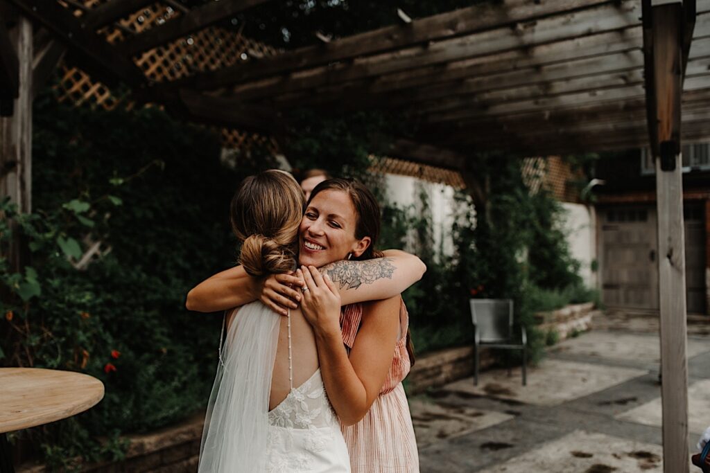 A bride hugs a guest during cocktail hour at their outdoor wedding venue