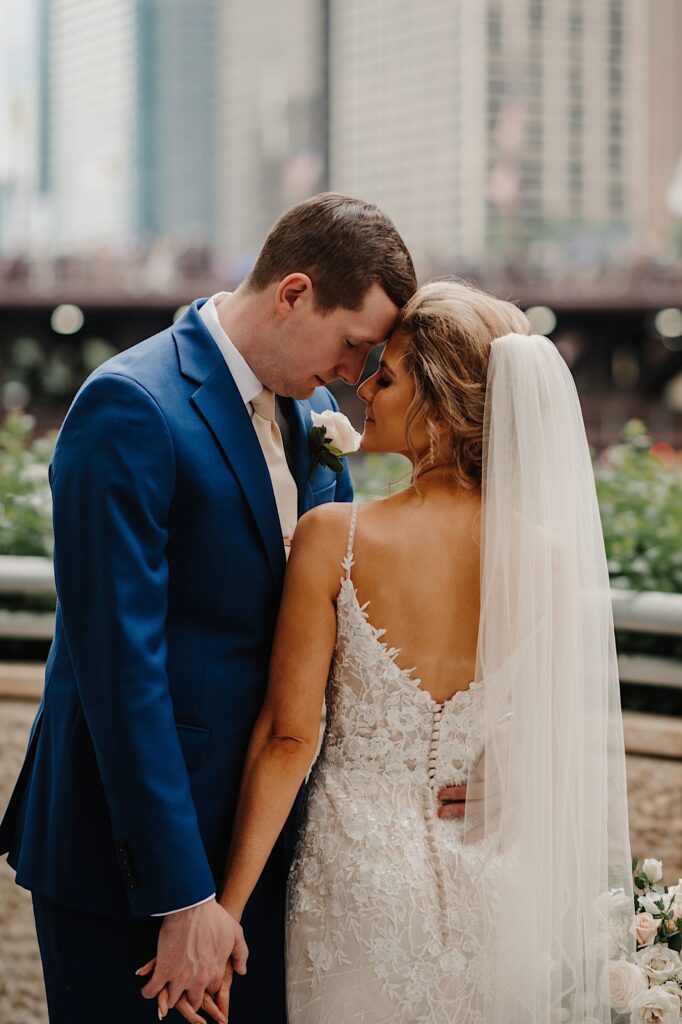 The bride and groom stand close together pressing their foreheads together standing on the Riverwalk in Chicago.