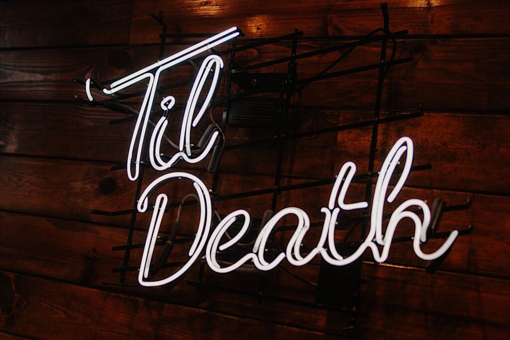 Neon sign that reads "til death" hanging on a wooden wall