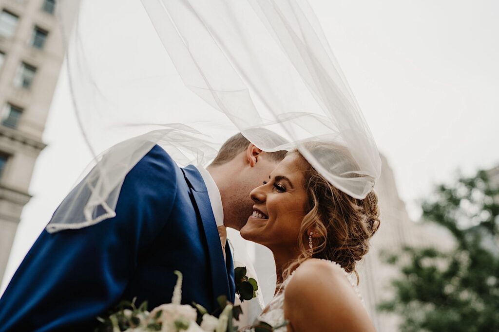 The bride and groom share an intimate moment together with their foreheads pressed together and their eyes closed.  They're tucked underneath the brides veil