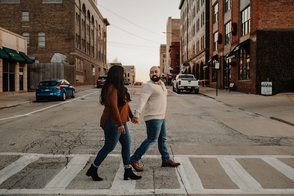 A couple walks across the street in a cross walk in downtown Bloomington Illinois during their fall engagement session.