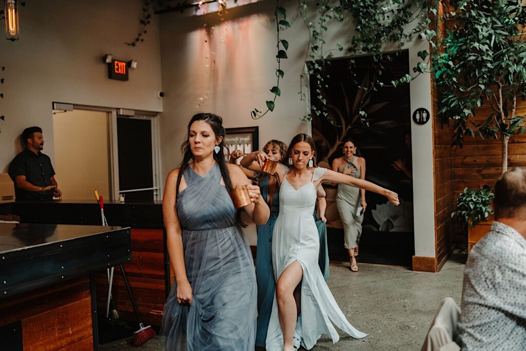 Bridesmaids enter the wedding reception space at Ivy House while dancing and laughing.