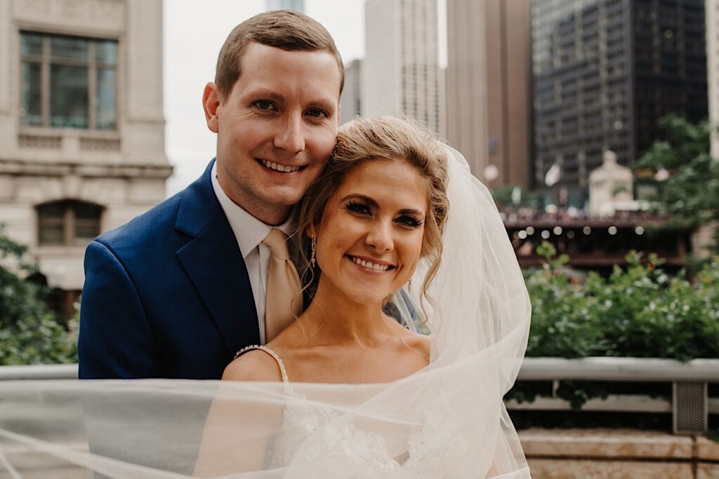 A bride and groom hold one another while smiling at the camera during their wedding portraits on the Chicago Riverwalk.