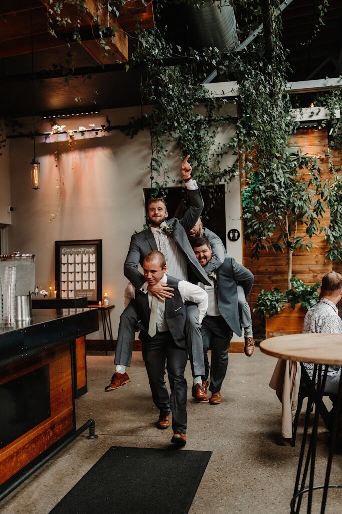 Groomsmen entering a wedding reception riding piggy back on one another while laughing and cheering