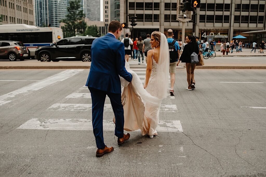 The groom carries his brides train while crossing Michigan Avenue in Chicago during their summer wedding day.