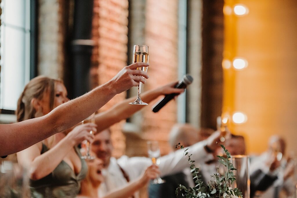 A microphone and a glass of champagne are extended outwards to toast to the newly wed couple at an indoor wedding reception at Ivy House