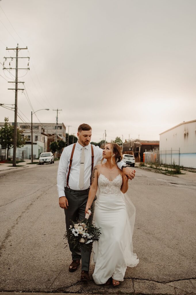 A bride and groom walk down the street together outside of their wedding venue after sneaking away during the reception for some portraits.