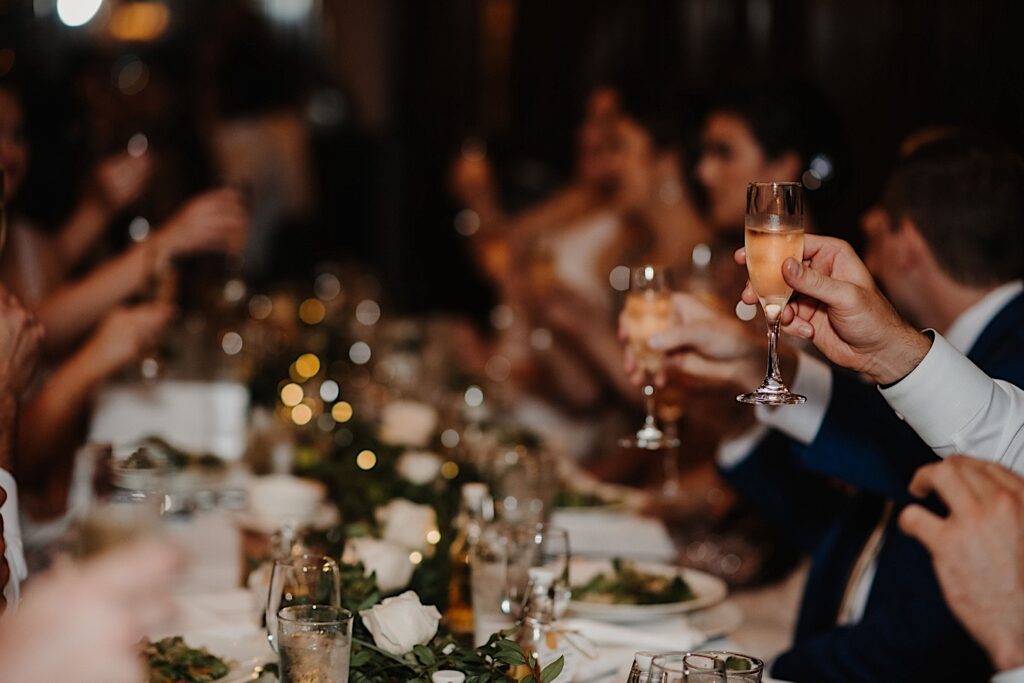 Guests of a wedding raise their glasses while sitting at a table decorated for a wedding reception.