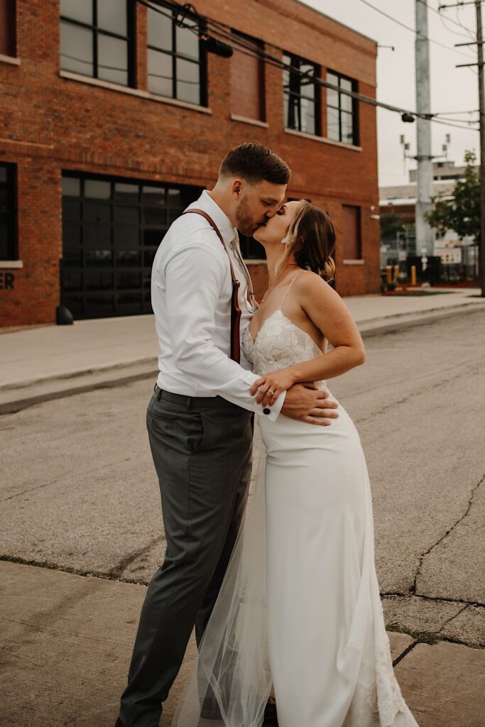 A bride and groom kiss in the street together outside of their wedding venue after sneaking away during the reception for some portraits.