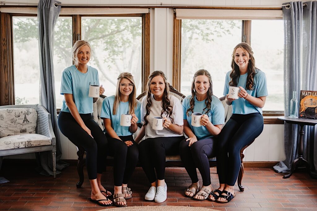 A bride and her bridesmaids holding matching cups and wearing matching bridesmaid shirts.