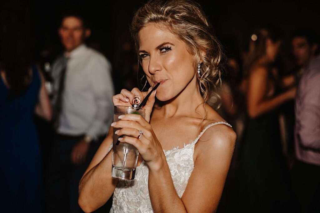 A bride drinks from a straw while smirking at the camera during her wedding reception at Salvatore's in Chicago