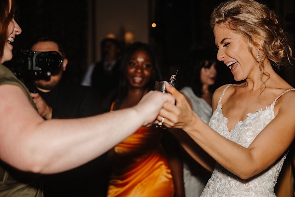 A bride smiles and laughs as she holds one of her friends hands while dancing during her wedding reception at Salvatore's in Chicago