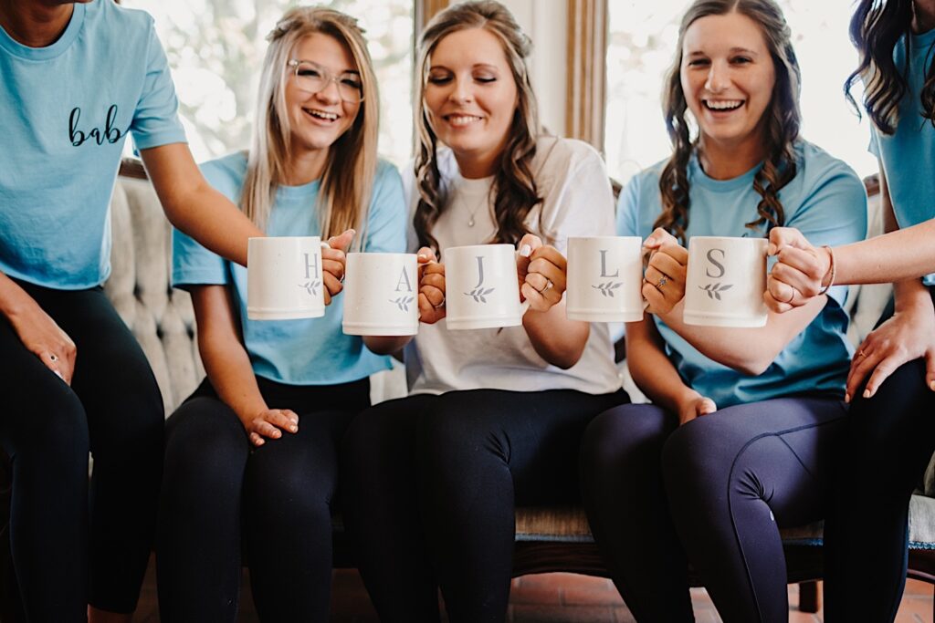 A bride and her bridesmaids holding matching cups and wearing matching bridesmaid shirts.  They are clinking their coffee cups together.