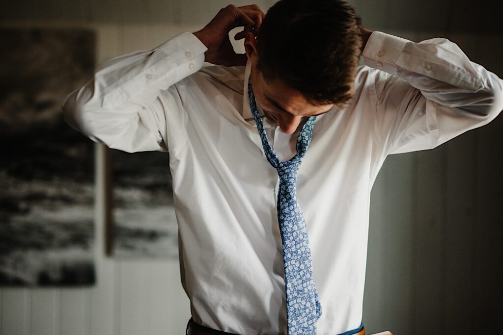 The groom puts on his blue floral wedding tie in the getting ready space at his Wisconsin wedding venue, 1841 Farms and Vineyard