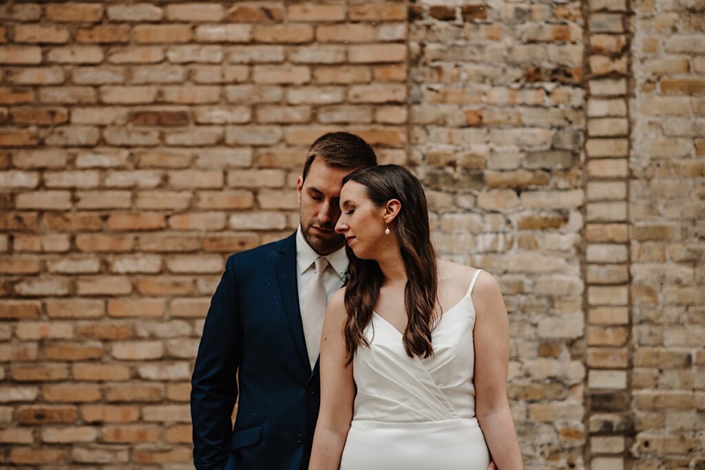 A couple stands with serious faces in front of an old brick wall outside of their Chicagoland wedding venue.