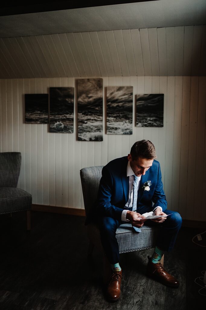 The groom unfolds a note from his bride sitting in his getting ready space in his Wisconsin wedding venue.