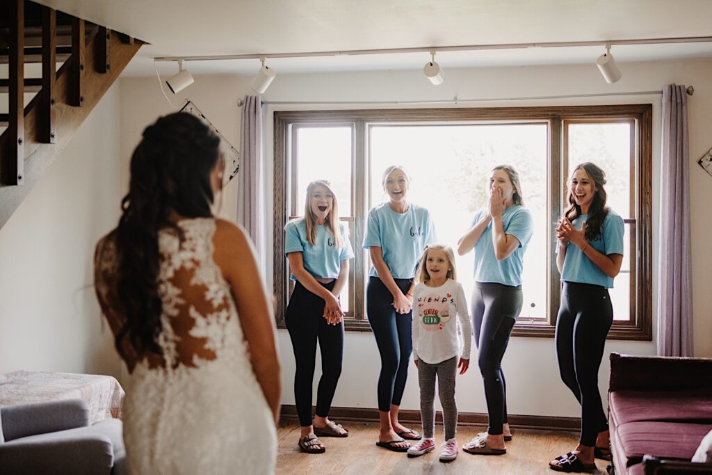 A bride has a first look with her bridesmaids in front of a window in the getting ready space at their Wisconsin wedding venue.