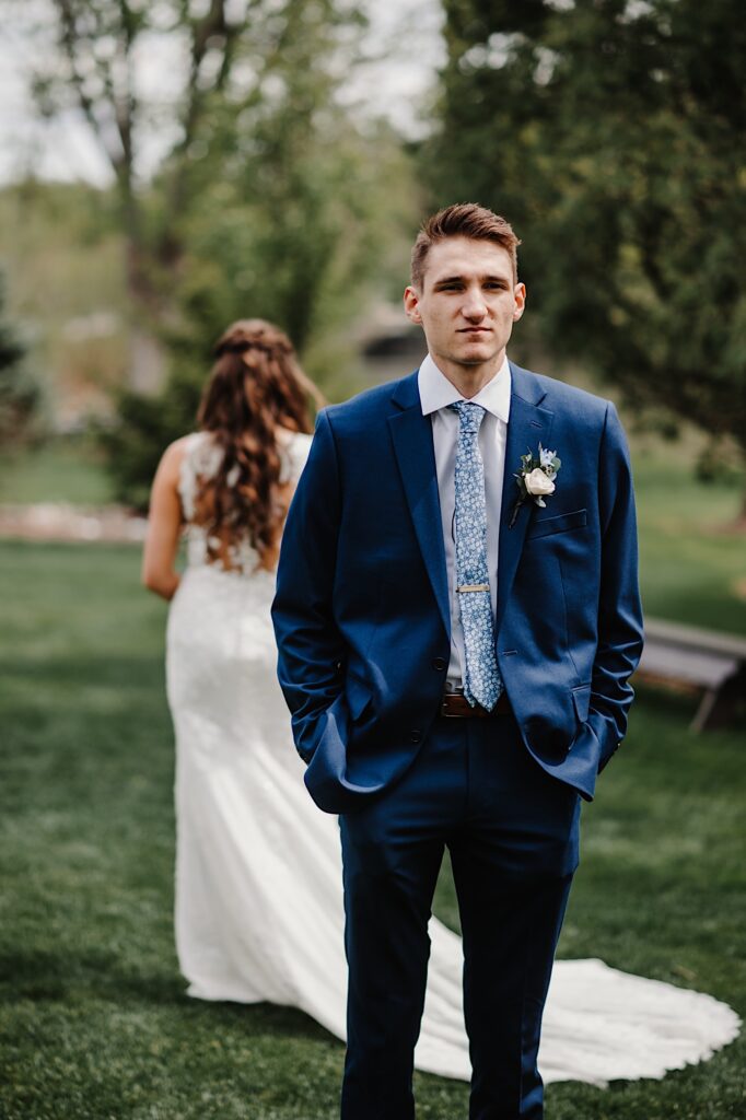 A photo of the groom standing facing away from his bride.  The bride and groom stand back to back before their first look at their wedding venue in Wisconsin.
