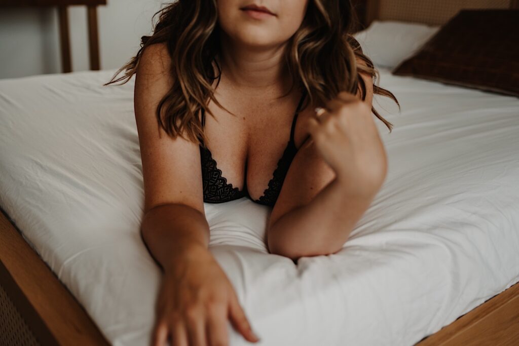 A close up image of a woman laying on her bed with her chest facing the camera with a scallop edged lace bra during her Chicago boudoir session.