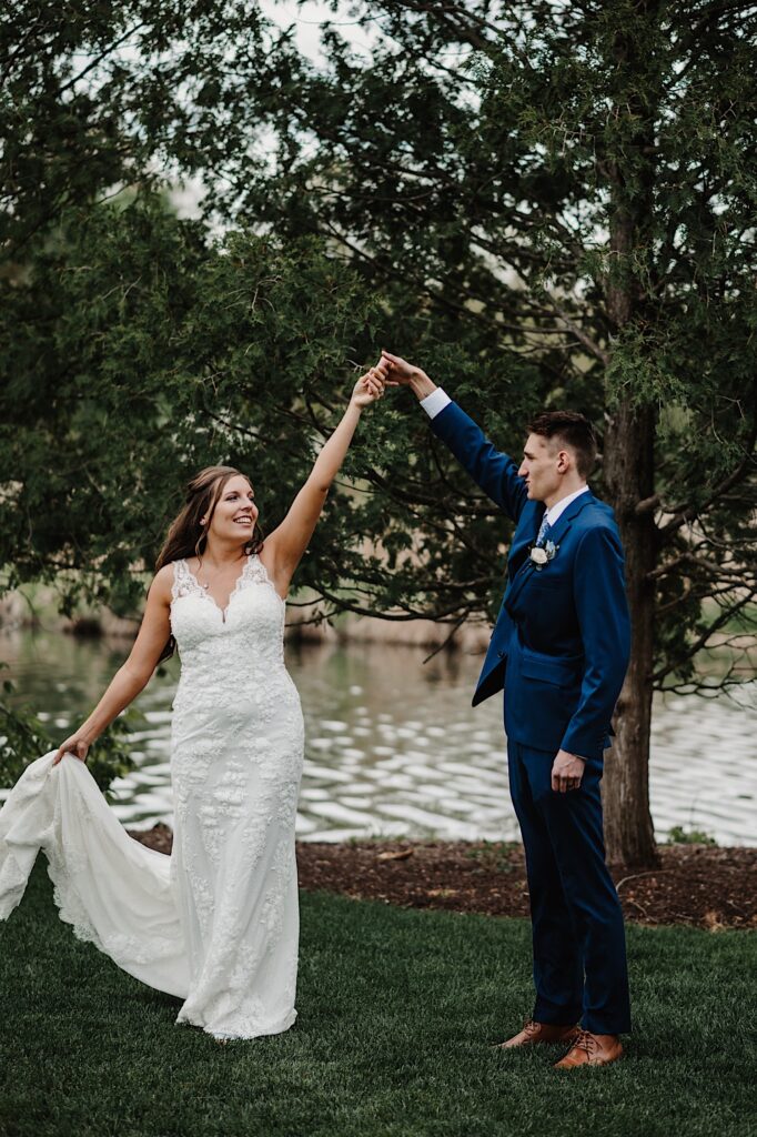A groom twirls his bride in front of a lake at their Wisconsin wedding venue, the 1841 Farms and Vineyard