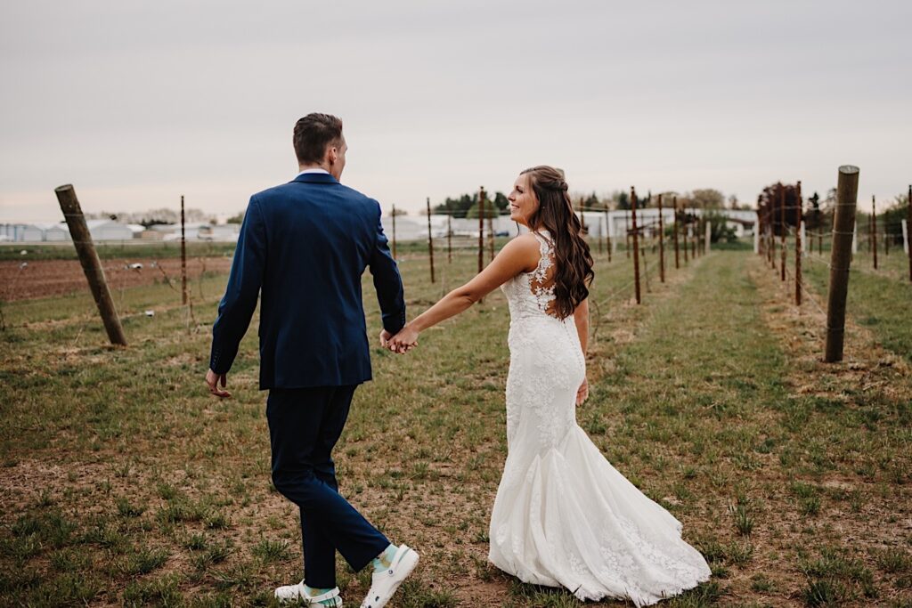 A bride and groom walk through the orchard at 1841 Farms and Vineyard during their Wisconsin wedding.