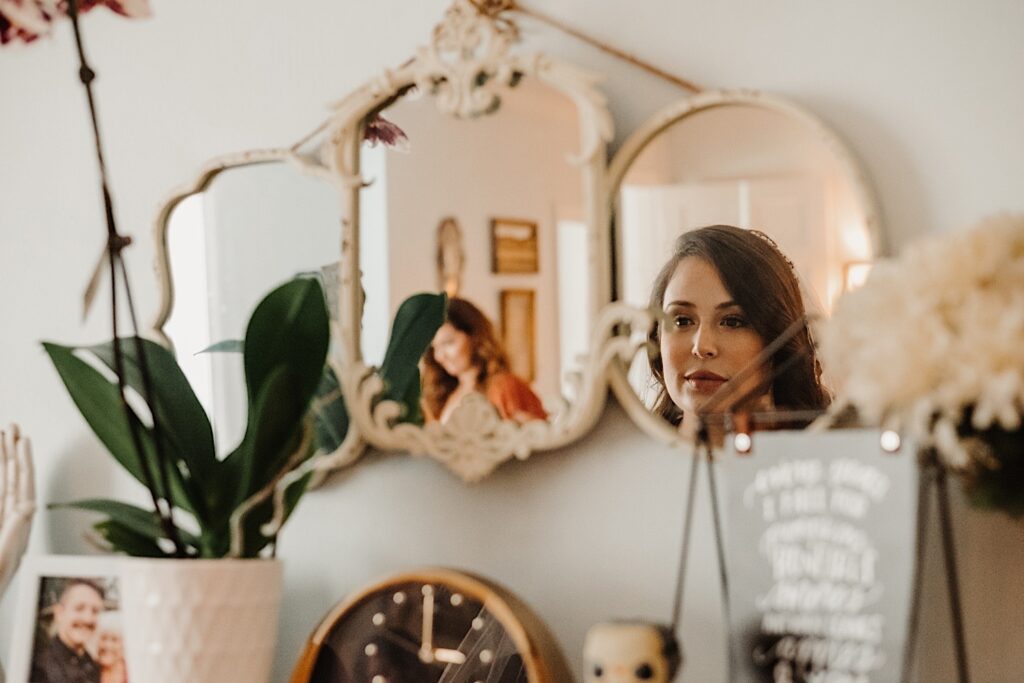 Photo of a mirror on the wall, in the mirror is a reflection of a woman staring at herself as she gets ready for her wedding day