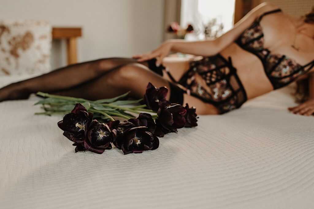 Detail photo of black flowers on a bed with a woman in lingerie out of focus behind the flowers