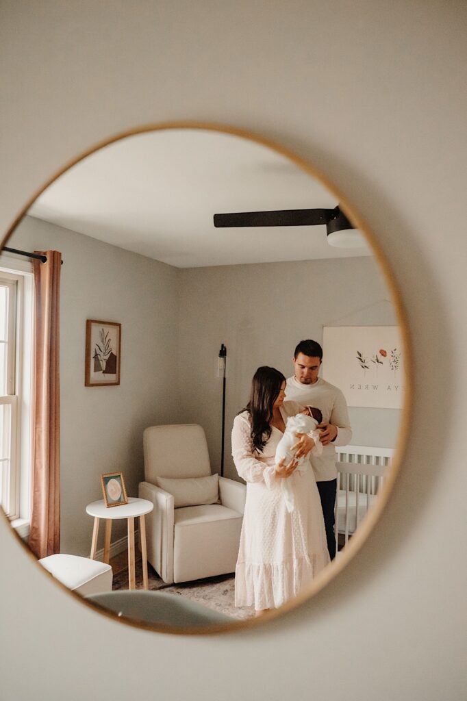 A Photo of a mirror with a father and mother in it holding and looking at their baby.