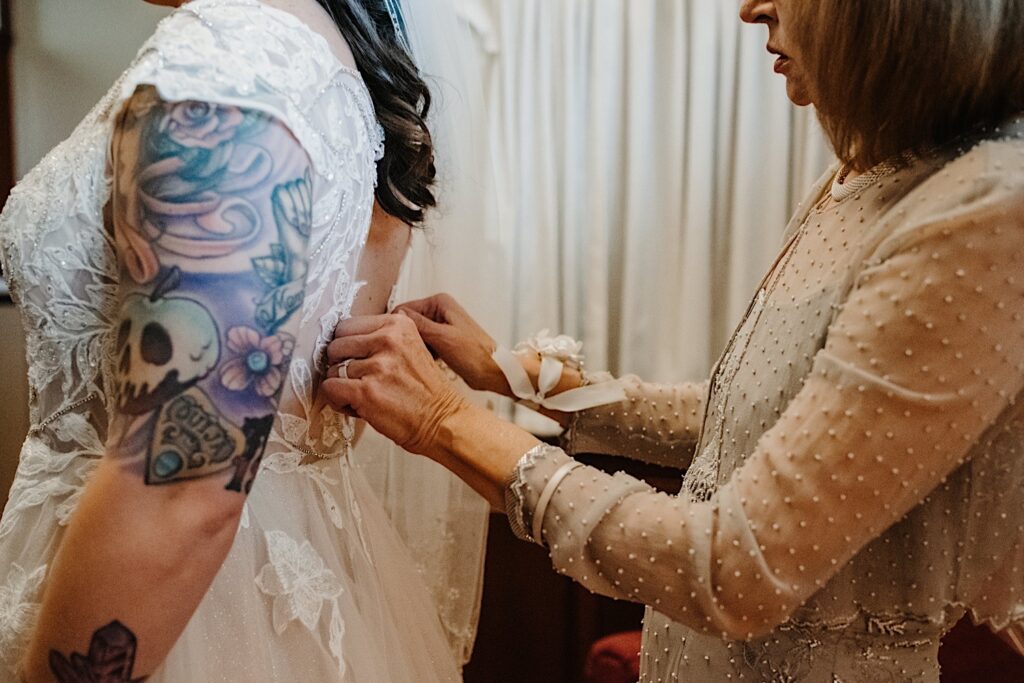 A woman helps button up the back of another woman's wedding dress