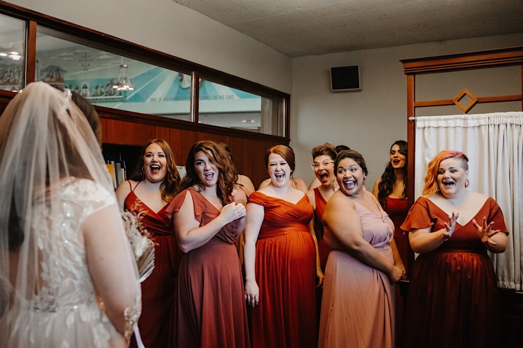 During a fall wedding in Chicago a bride stands with her back to the camera as her bridesmaids all turn and react seeing her for the first time in her dress