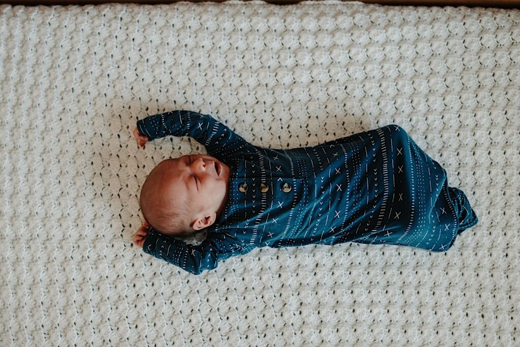 An infant in blue pajamas stretches their arms up while sleeping.