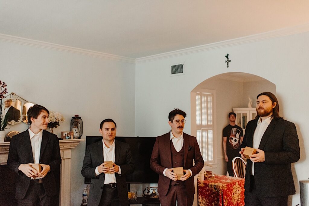 A groom stands with three of his groomsmen while giving a speech before his fall wedding day in Chicago, each of them holds a small brown box