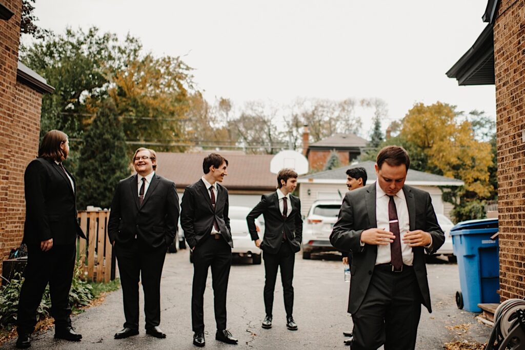 Six groomsmen stand in a Chicago driveway in the fall talking and adjusting their suits before making their way to the wedding ceremony